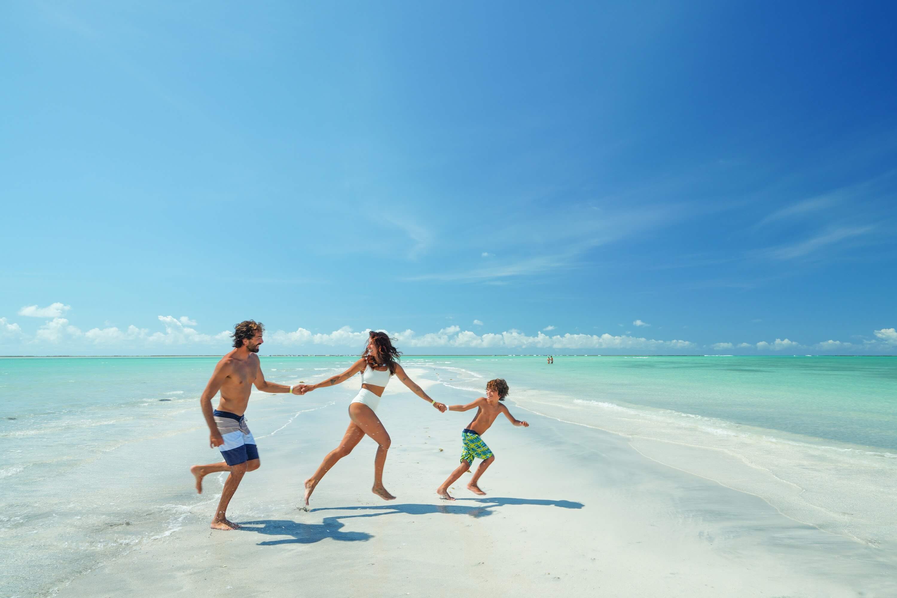 Família feliz correndo em banco de areia no meio do mar da Praia de Antunes.